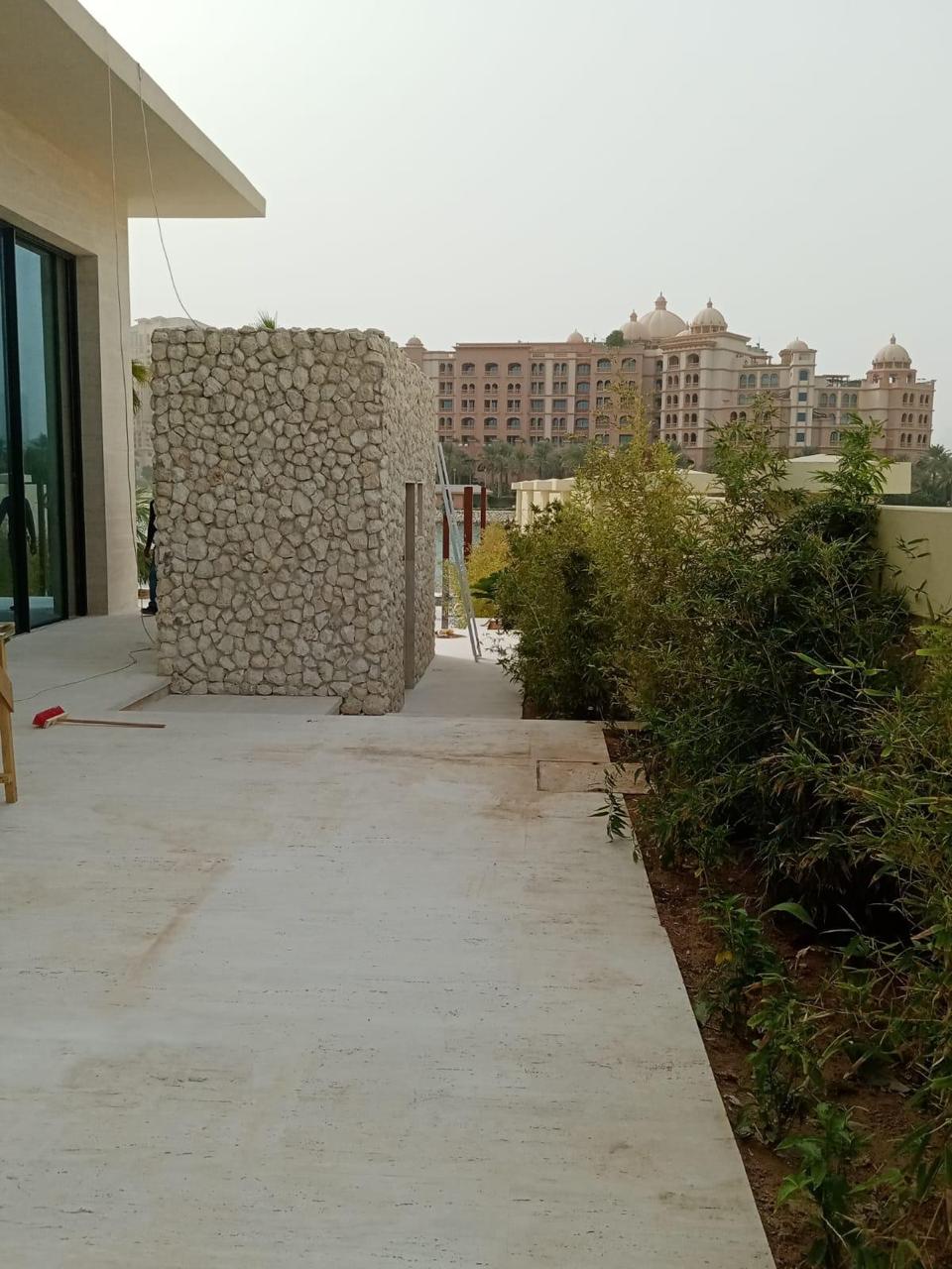 SpaceForge exterior landscaping fit-out Dubai, villa garden terrace with pebble-clad feature wall, planted greenery, and views of the surrounding neighbourhood