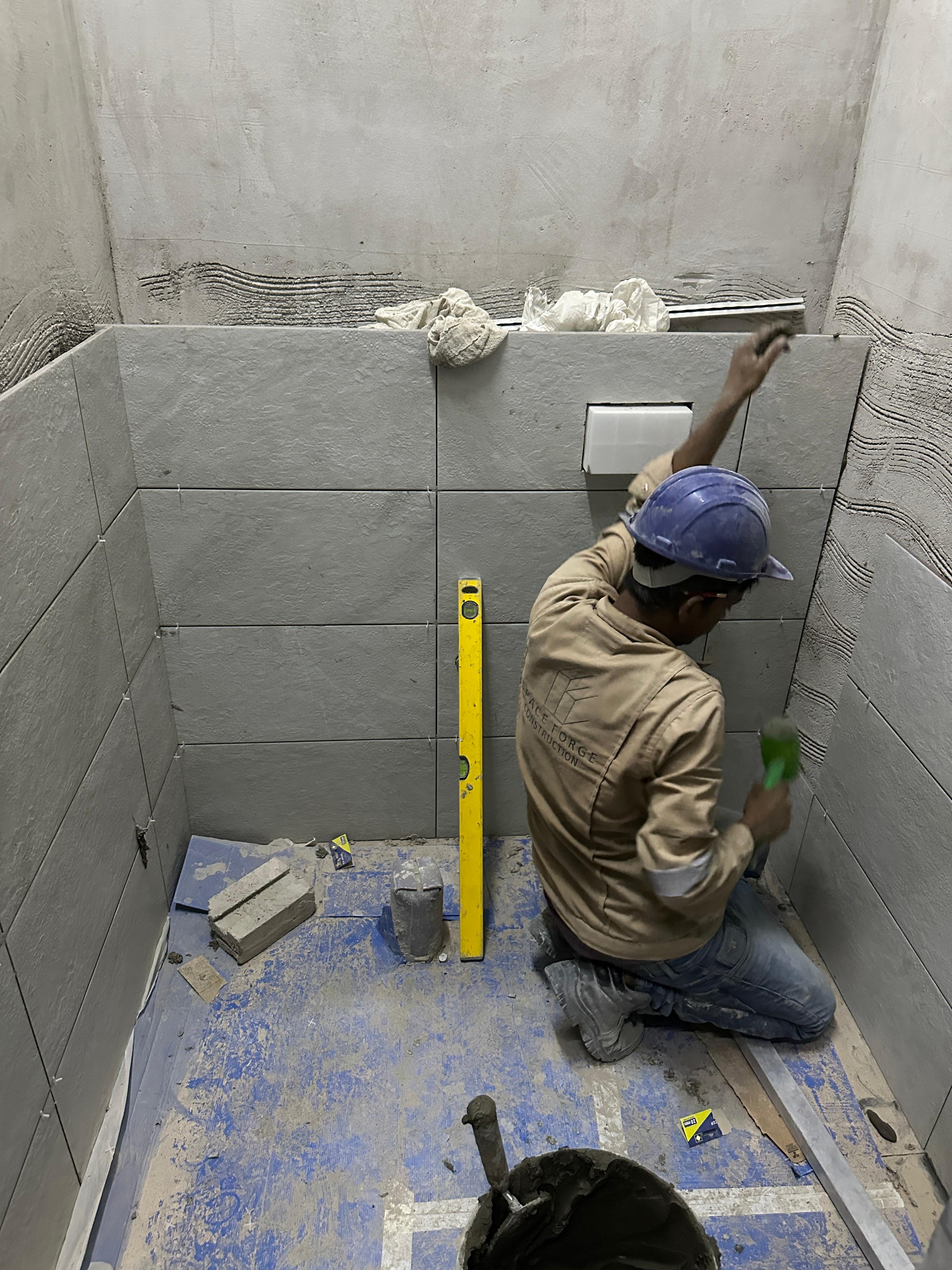 SpaceForge bathroom fit-out Dubai, craftsman applying precision wall tiling with a spirit level inside a luxury residential bathroom